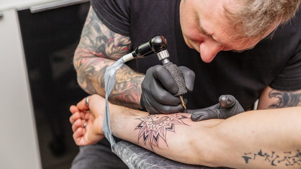 Tattoo artist applying flower tattoo on arm scar