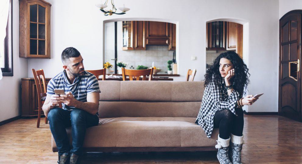 Couple in conflict sitting on sofa at home, using smart phones