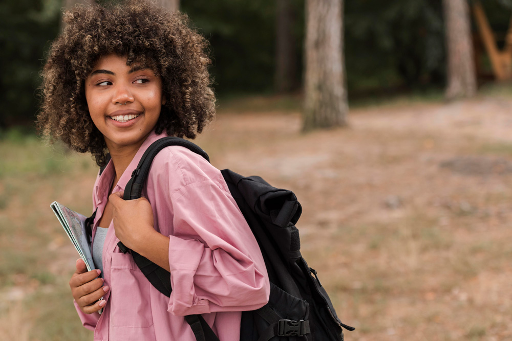 A teen with a backpack stands confidently in a grassy area